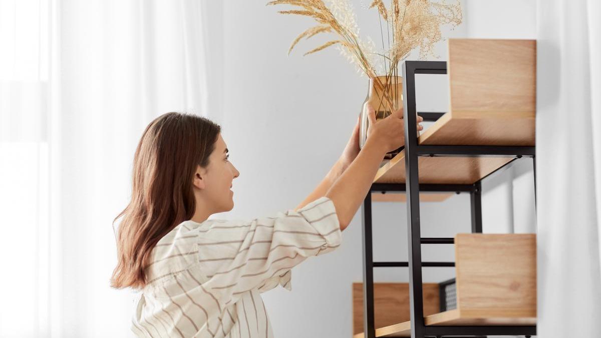 Chica coloca un jarrón decorativo en una estantería del salón.
