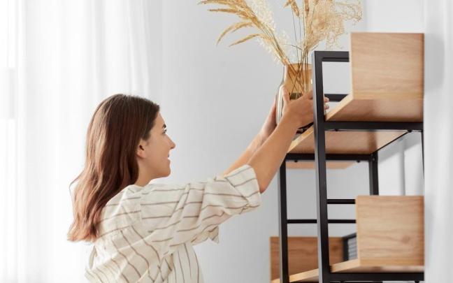 Chica coloca un jarrón decorativo en una estantería del salón.