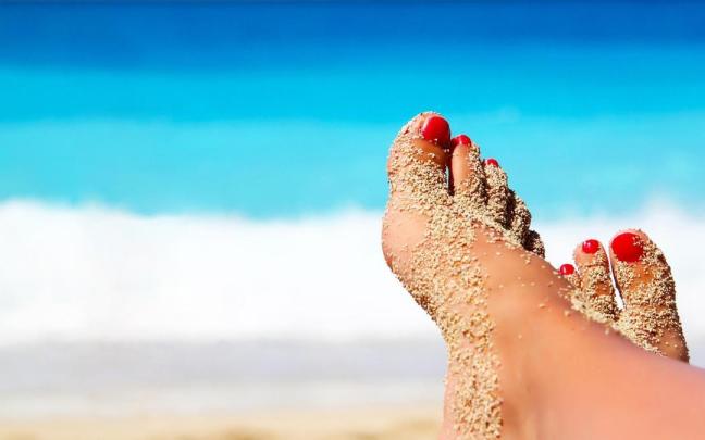 Una mujer toma el sol en la playa con los pies cubiertos de arena. Una mujer toma el sol en la playa con los pies cubiertos de arena.