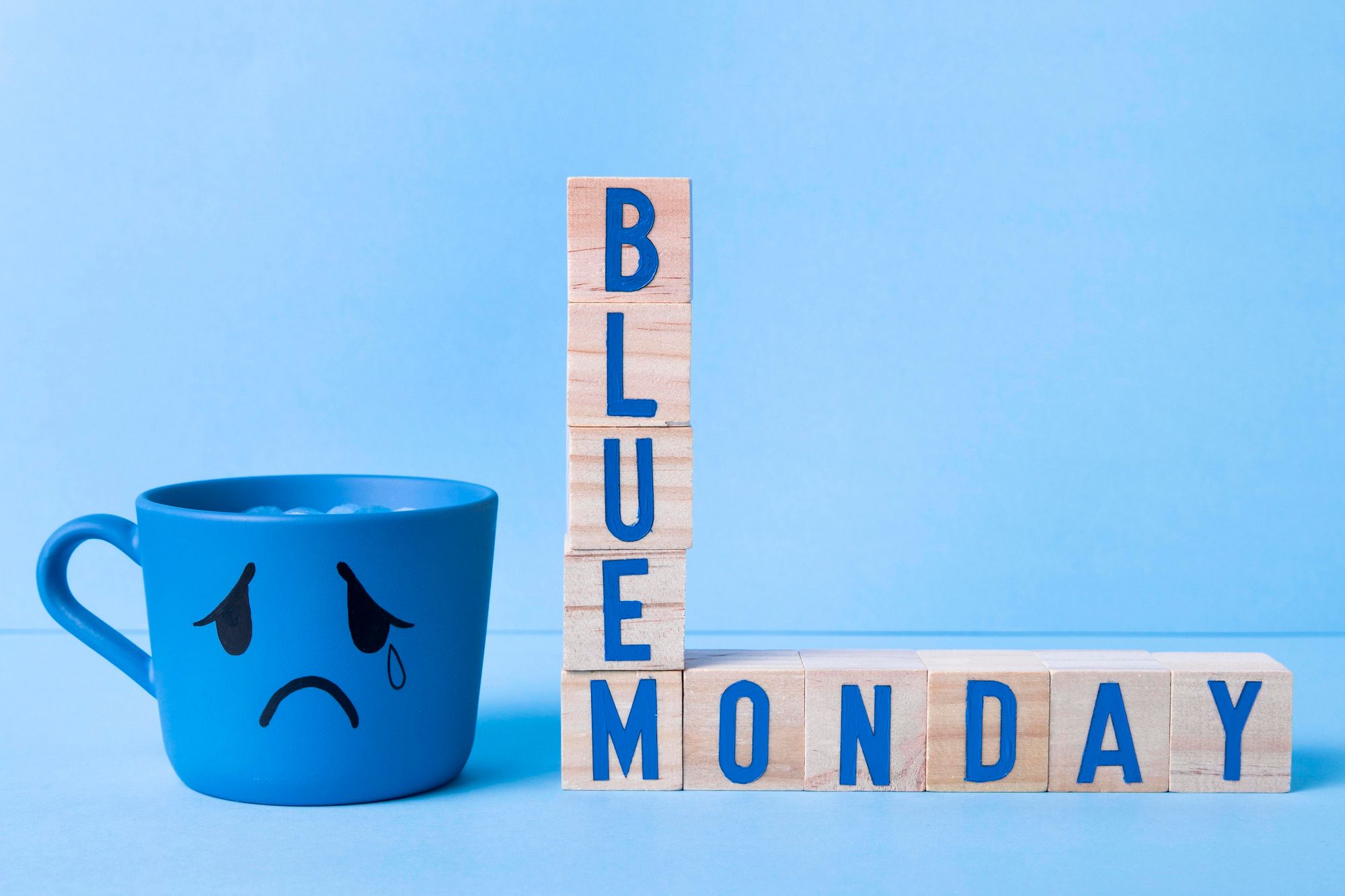 Una taza con gesto triste junto a unas piezas de madera en las que se lee 'Blue Monday'.