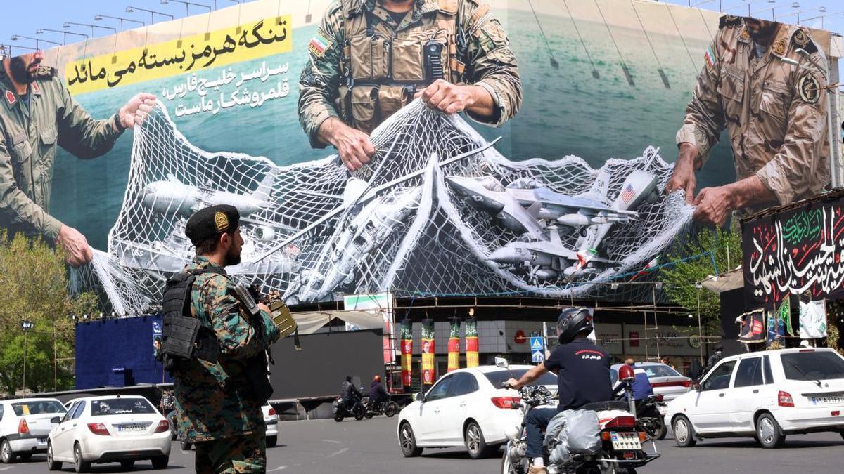 Un soldado iraní vigila el tráfico que pasa junto a una enorme valla publicitaria con el mensaje "El estrecho de Ormuz permanecerá cerrado", en Teherán.