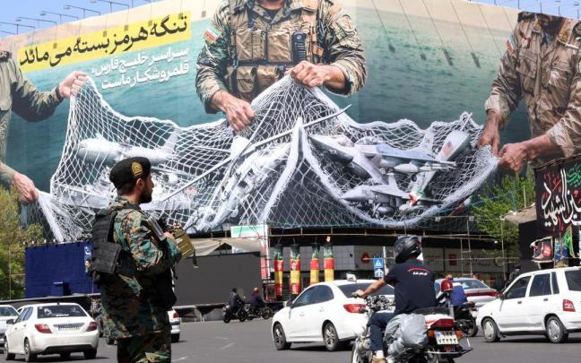 Un soldado iraní vigila el tráfico que pasa junto a una enorme valla publicitaria con el mensaje 