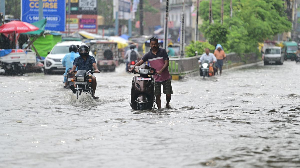 Varias motos tratan de circular por una carretera cubierta por el agua en la India.