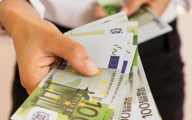 Una persona sostiene un fajo de billetes de 100 euros en su mano.