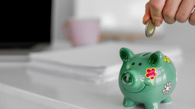 Una persona mete una moneda de euro en una hucha con forma de cerdito.