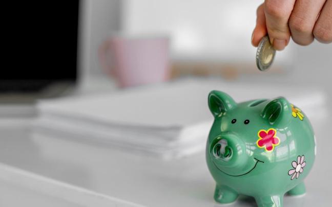 Una persona mete una moneda de euro en una hucha con forma de cerdito.