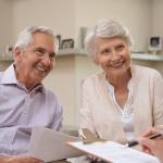 Pareja de personas mayores sonríen en una conversación con su asesora financiera.
