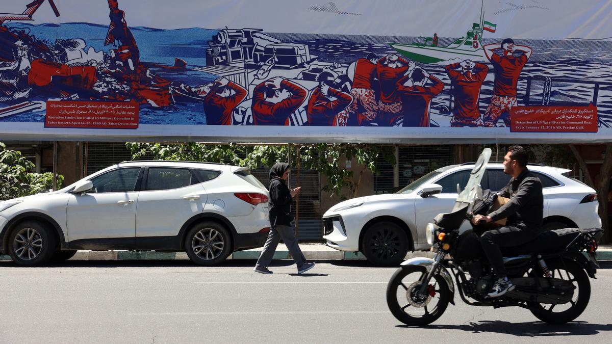 Iraníes pasan junto a una valla publicitaria contra EE.UU. cerca de la antigua embajada estadounidense en Teherán.