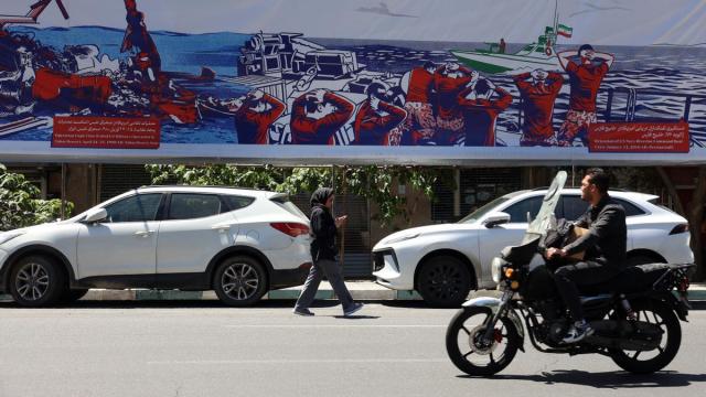 Iraníes pasan junto a una valla publicitaria contra EE.UU. cerca de la antigua embajada estadounidense en Teherán.