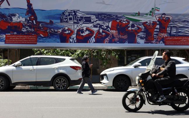 Iraníes pasan junto a una valla publicitaria contra EE.UU. cerca de la antigua embajada estadounidense en Teherán.