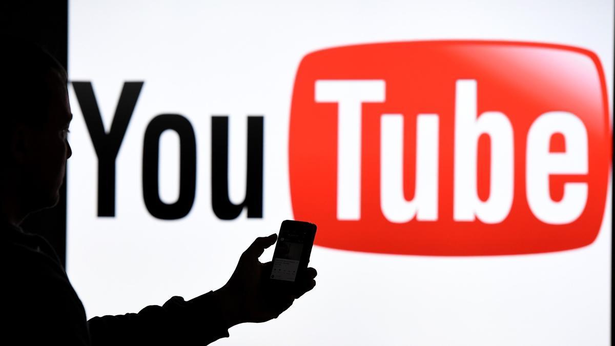 Un usuario usa el móvil frente al logo de YouTube.