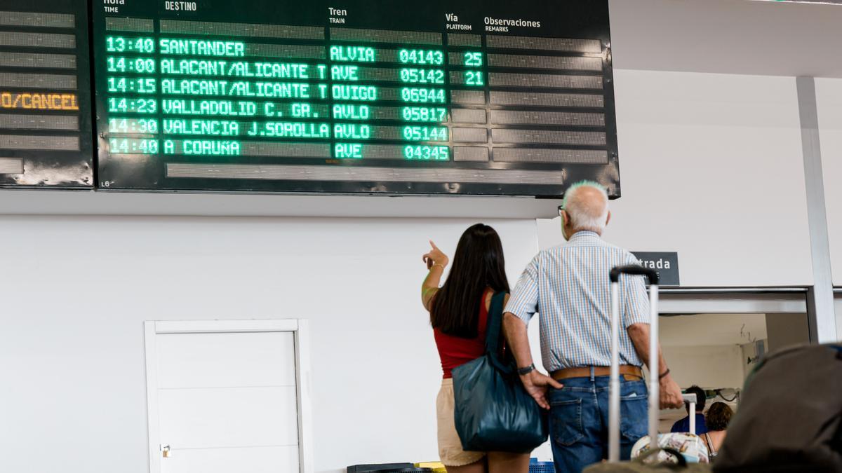 Varias personas esperan con maletas, junto a los carteles de salidas