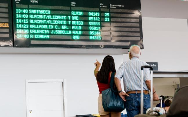 Varias personas esperan con maletas, junto a los carteles de salidas
