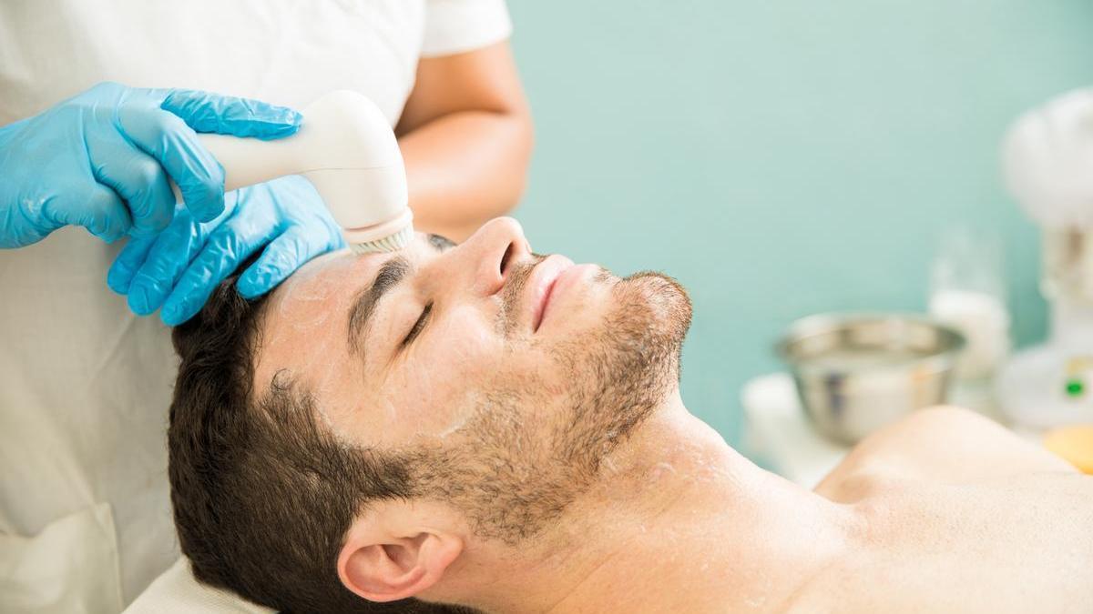 Hombre joven recibe una limpieza facial profesional en un centro especializado de medicina estética.
