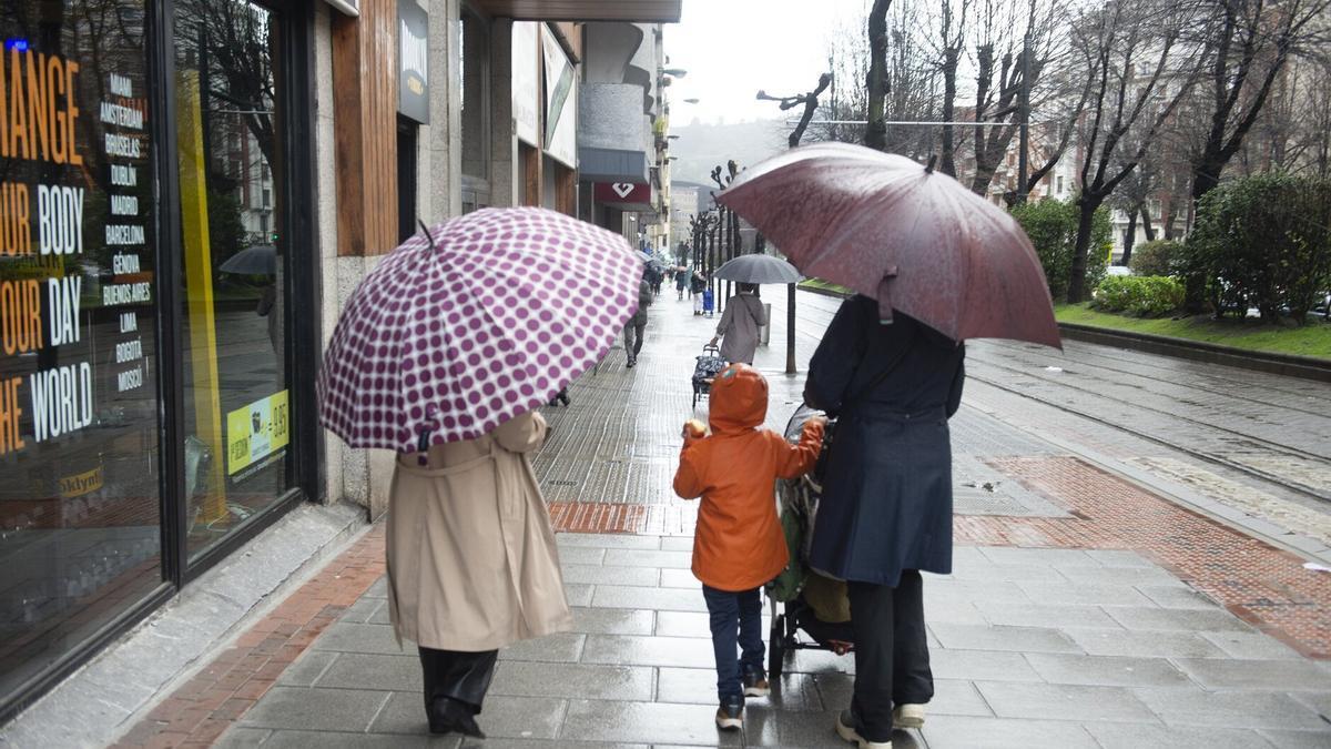 Una familia se refugia de la lluvia con paraguas y abrigos.