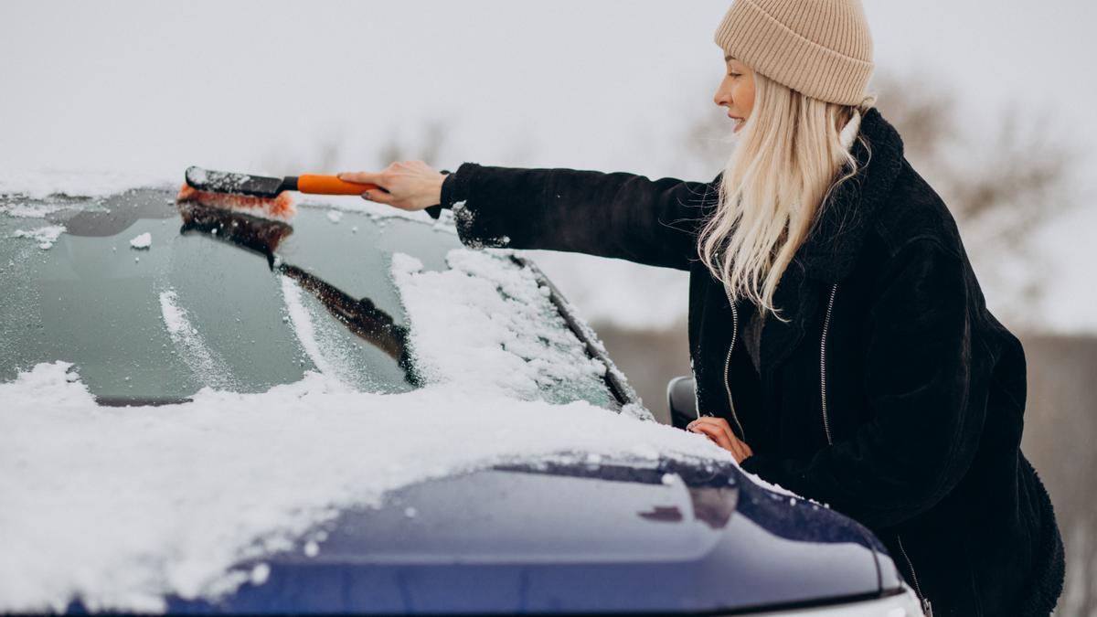 Una joven retira la nieve del coche con una rasqueta.