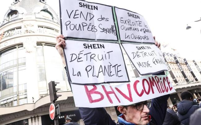 Un hombre levanta un cartel de protesta contra Shein en la inauguración de su primera tienda física en parís.
