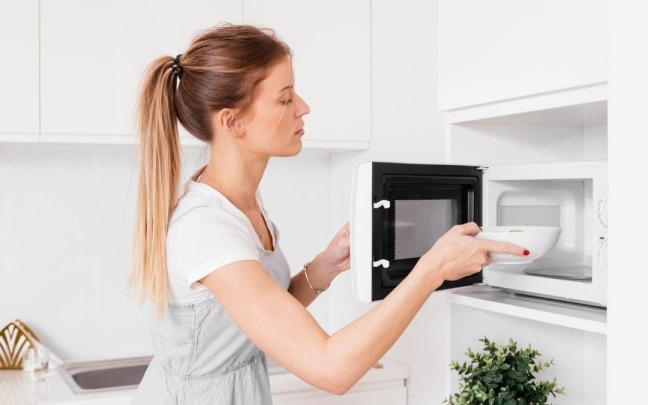 Una mujer se dispone a calentar un cuenco de cerámica con comida en el microondas. Una mujer se dispone a calentar un cuenco de cerámica con comida en el microondas.