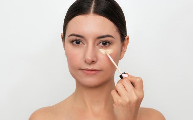 Una mujer se aplica corrector en las ojeras.