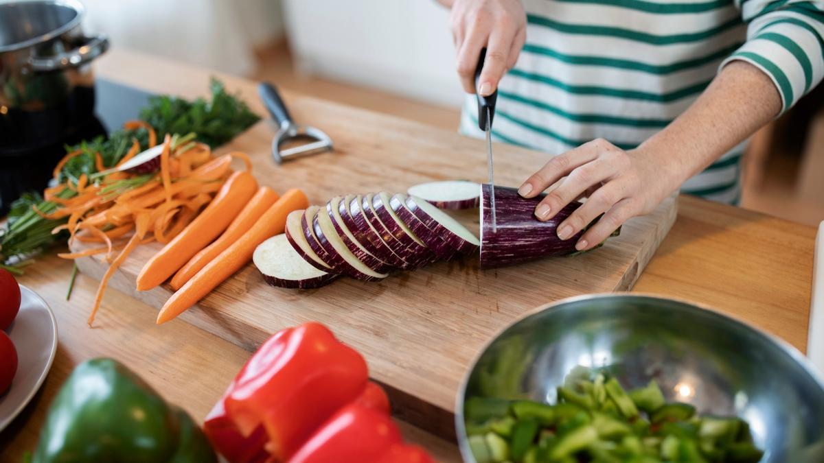 Una mujer corta en rodajas varias hortalizas para preparar una receta.