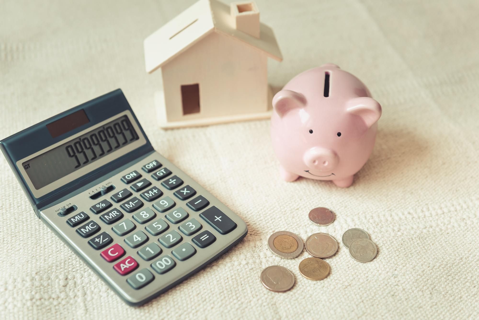 Una calculadora, una hucha y una casita de madera, junto a un puñado de monedas.