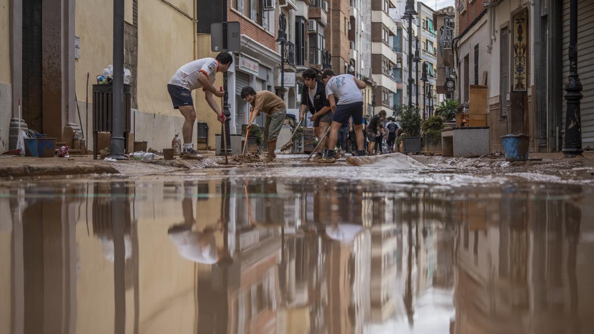 Un grupo de jóvenes trata de quitar el agua acumulada en las calles.
