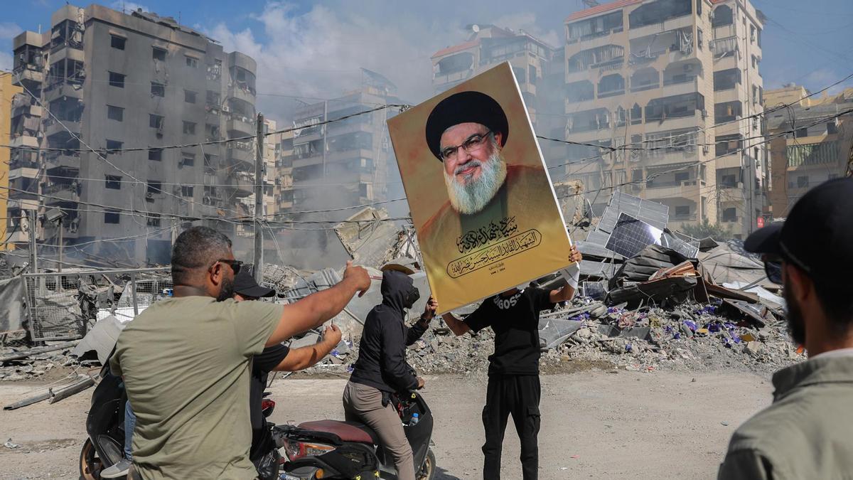 Un seguidor de Hizbulá sostiene un cartel con la imagen del fallecido Hassan Nasrallah ante un edificio destruido en Beirut.