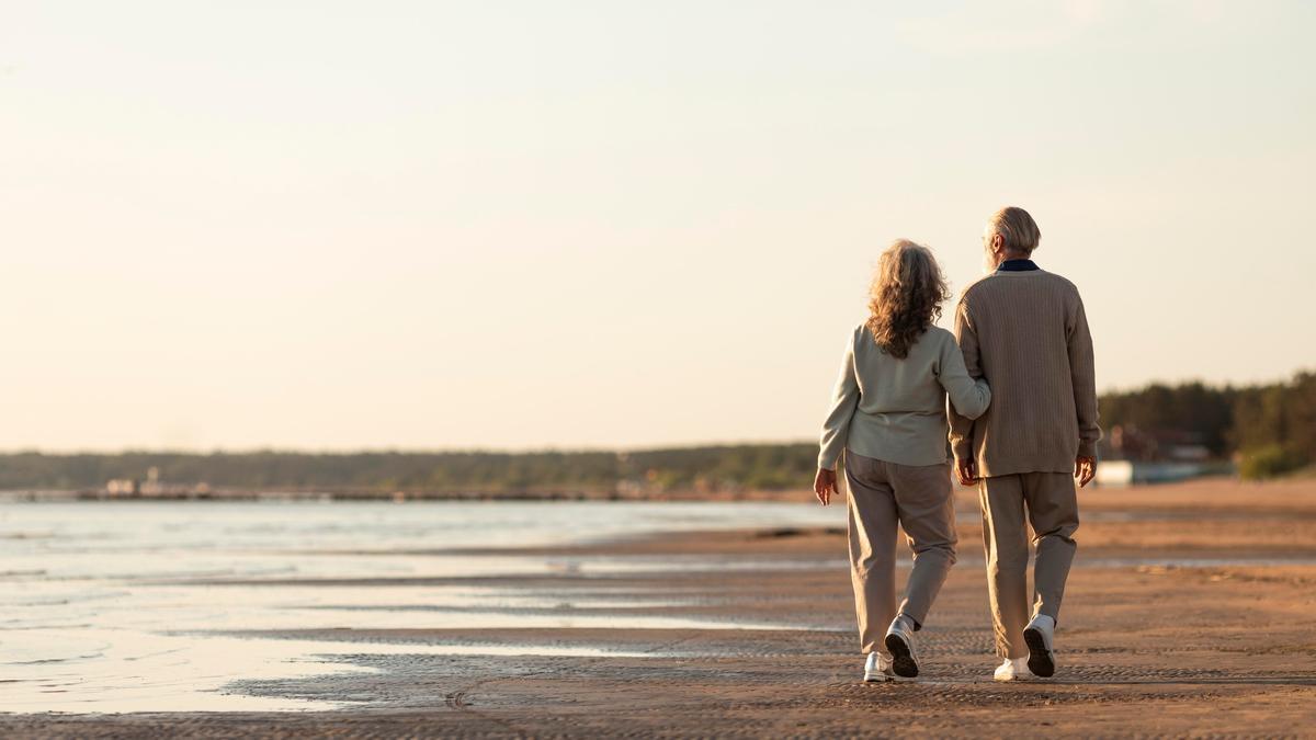 Una pareja de jubilados pasea por la orilla del mar.