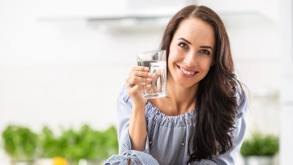 Una mujer sonríe mientras sostiene un vaso de agua.
