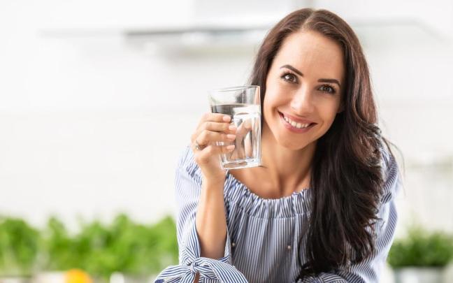 Una mujer sonríe mientras sostiene un vaso de agua. Una mujer sonríe mientras sostiene un vaso de agua.