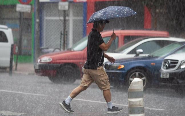 Un hombre se cubre de la lluvia intensa con un paraguas.
