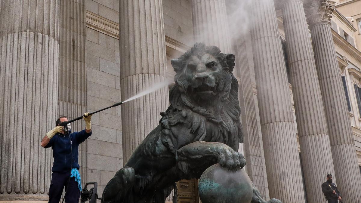 Un operario limpia con una manguera a presión uno de los leones del Congreso de los Diputados.