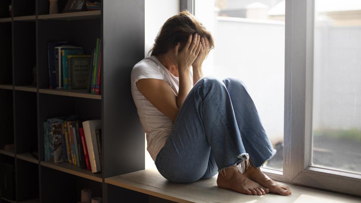 Mujer sentada bajo la ventana con un episodio de ansiedad.