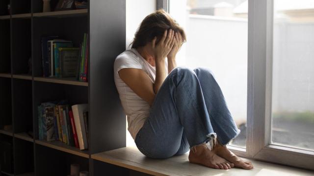 Mujer sentada bajo la ventana con un episodio de ansiedad.