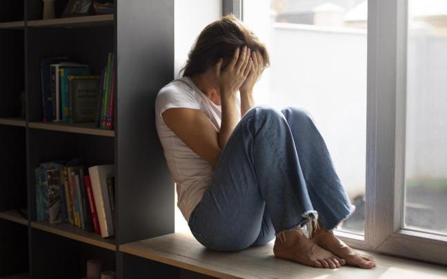 Mujer sentada bajo la ventana con un episodio de ansiedad.