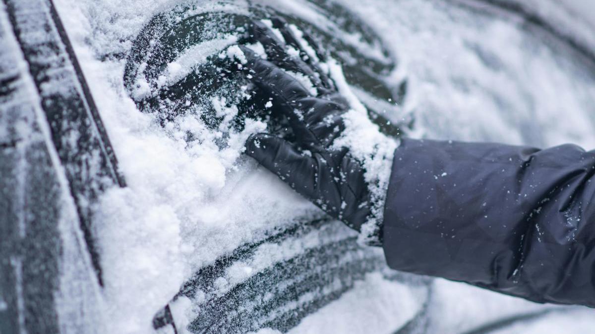 Mano de un conductor tratando de eliminar el hielo de los cristales del coche