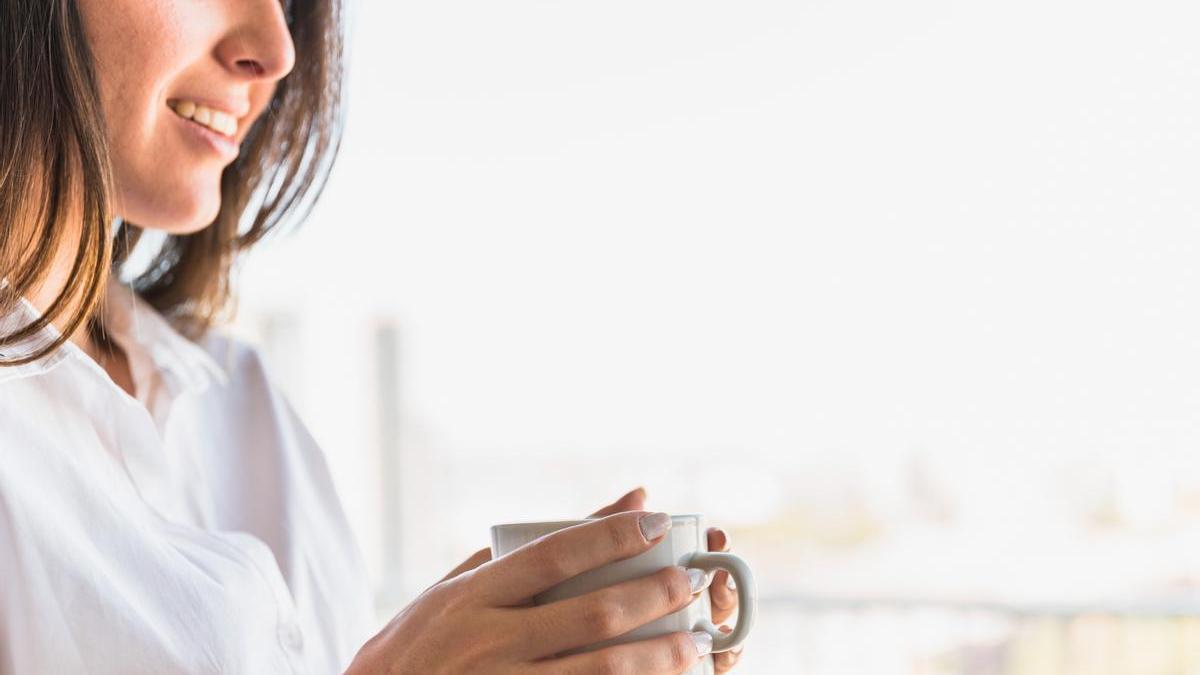 Mujer con una sonrisa sostiene una taza de café