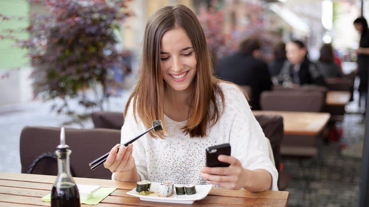 Imagen de archivo de una chica usando el móvil en un restaurante