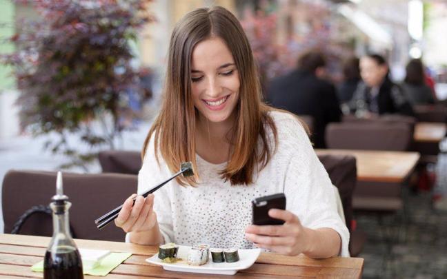 Imagen de archivo de una chica usando el móvil en un restaurante