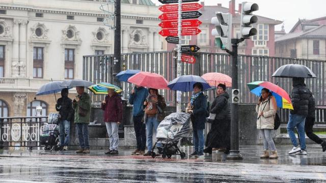 Un grupo de personas espera en un paso de cebra bajo la lluvia en Bilbao.