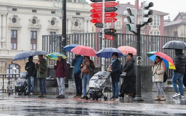 Un grupo de personas espera en un paso de cebra bajo la lluvia en Bilbao.