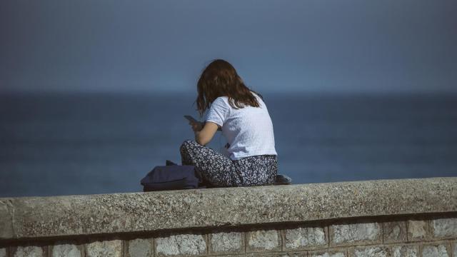 Una chica sentada sola frente al mar mirando su móvil.