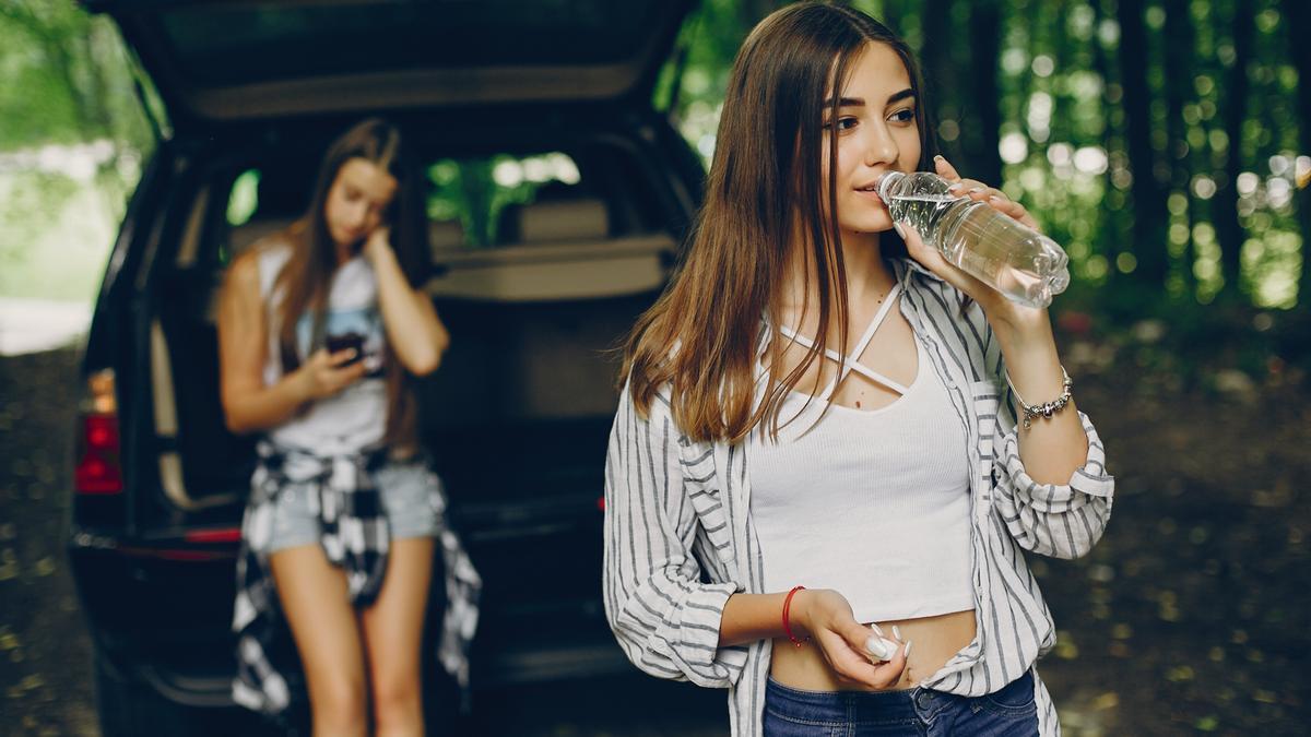 Chica joven bebe agua con su vehículo detenido.