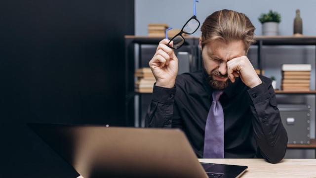 Un hombre se frota los ojos ante la pantalla de un portátil.
