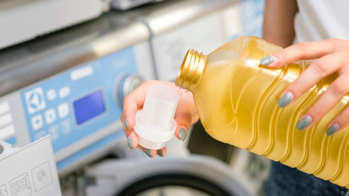 Una mujer, a punto de verter detergente de una botella en el tapón medidor.