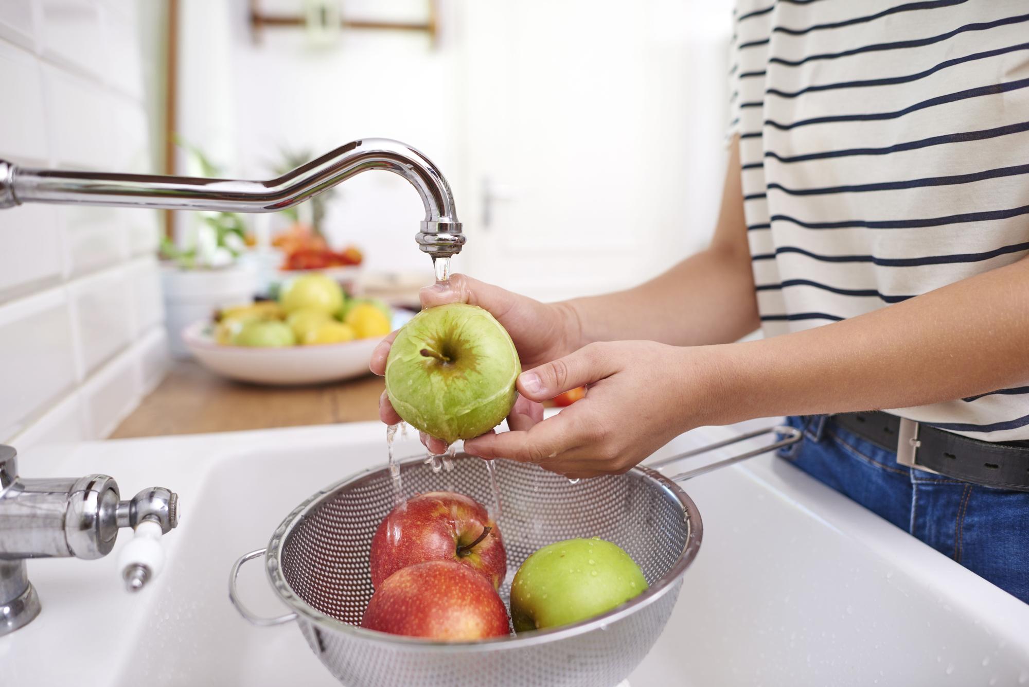 Mujer lava cuidadosamente las manzanas en la fregadera.