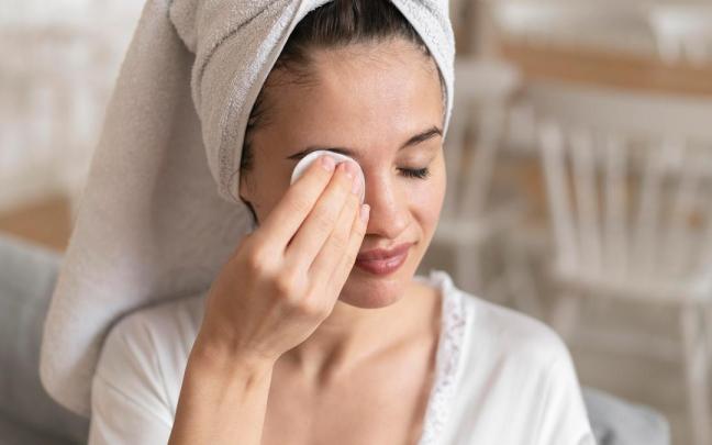 Una mujer se desmaquilla los ojos con un disco de algodón.