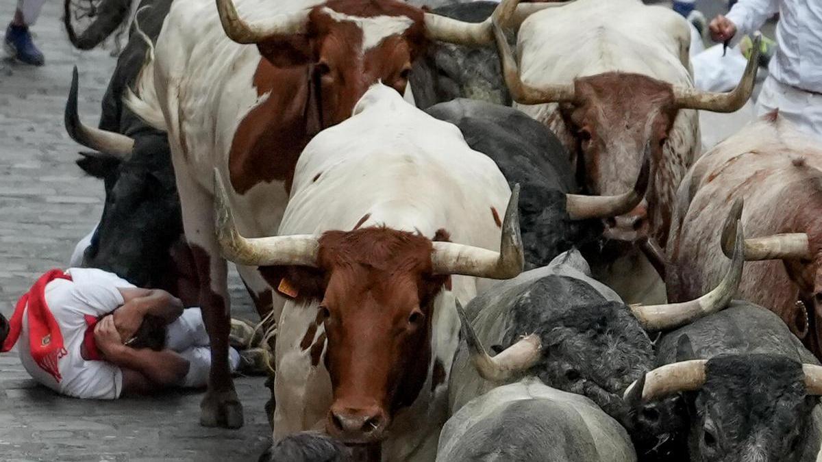 Un mozo en el suelo al paso de los toros de la ganadería de José Escolar Gil durante el último encierro de los Sanfermines 2024.