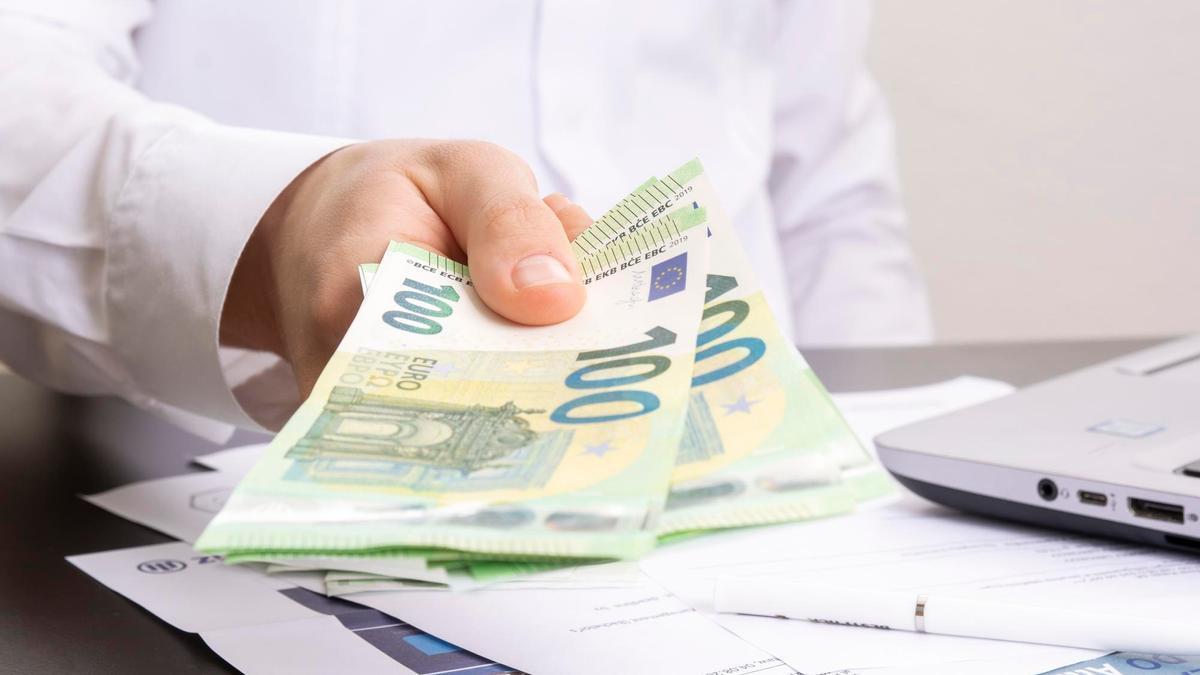 Una persona realiza un pago en una oficina con varios billetes de 100 euros.