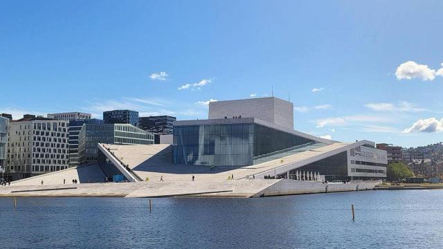 Panorámica del edificio de la Ópera sobre las aguas del fiordo, donde se ven las pequeñas figuras humanas a modo de oscuros pingüinos.